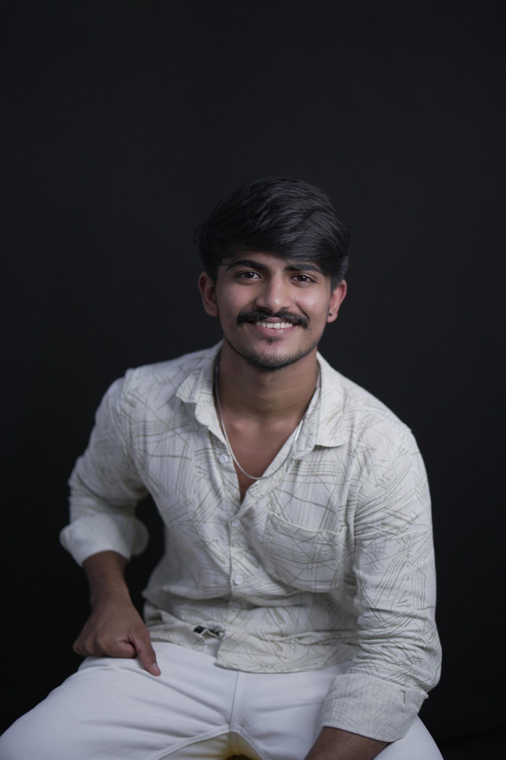 Portrait of Aromal, a freelance digital marketer in Calicut, sitting against a dark background and smiling at the camera. He is wearing a light patterned shirt and white pants, looking confident and professional.